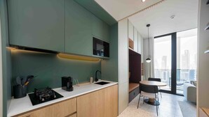 Una cocina moderna con estufa integrada, un lavamanos y cafetera. Hay un comedor con mesa y sillas, y vistas a la ciudad a través de amplios ventanales.