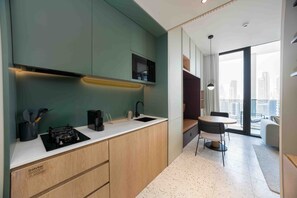 A modern kitchen with a built-in stove, a sink, and a coffee maker. There is a dining area with a table and chairs, and a view of the city through large windows. - Vibrant Studio w/ Burj View & Balcony (Dubai)