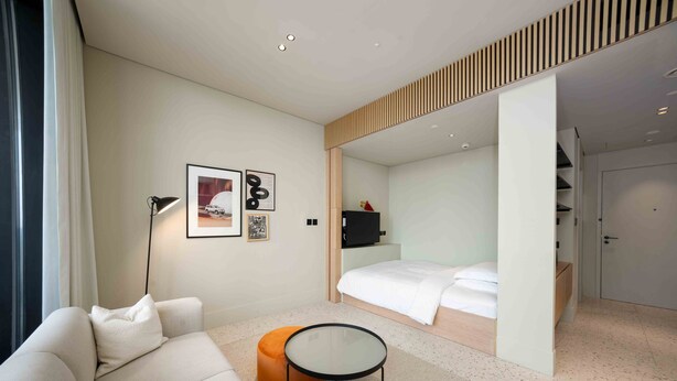 Una habitación de hotel moderna con sofá, una mesita redonda, cama y televisión.