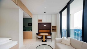 Una habitación de hotel moderna con sofá, una mesa redonda, zona de comedor y vistas a la ciudad.
