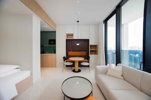 A modern hotel room with a sofa, a round table, a dining area, and a view of the city. - Vibrant Studio w/ Burj View & Balcony (Dubai)