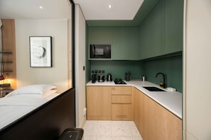 Ein kleines Hotelzimmer mit Bett, einer Küchenzeile, einem gerahmten Bild und einem kleinen Fenster.