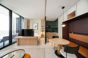 A modern hotel room with a large TV, a balcony with a view, a kitchen area, and a dining space. - Urban Upside Studio Near Downtown (Dubai)