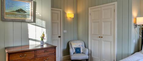 A bedroom with a wooden dresser, a chair, a bed, and a painting on the wall.