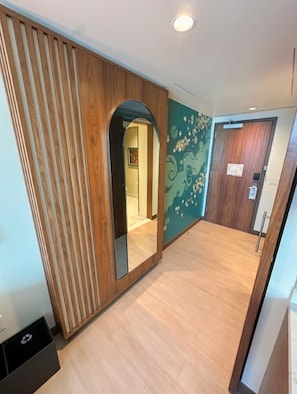 A hallway with a wooden panel wall, a mirror, a door with a wooden frame, and a wall with a floral pattern.
