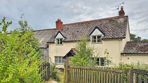 A two-story house with a thatched roof, a wooden fence, and a garden. - Historic Cornish Valley Cottage for 5 (Crediton)