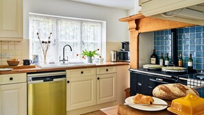 A kitchen with a Siemens dishwasher, a window with floral curtains, a wooden countertop, and a blue tiled backsplash. - Historic Cornish Valley Cottage for 5 (Crediton)