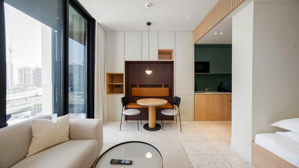 A modern hotel room with a sofa, a round table, a kitchenette, and a view of the cityscape. - Sleek Business Bay Studio | Burj View (Dubai)