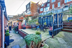 A residential courtyard with a brick house, a blue metal fence, potted plants, and outdoor furniture. - Seaside Cottage Near Whitby Abbey (Whitby)