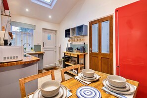 A compact kitchen with a dining area, featuring a microwave, sink, and wooden cabinets. - Seaside Cottage Near Whitby Abbey (Whitby)
