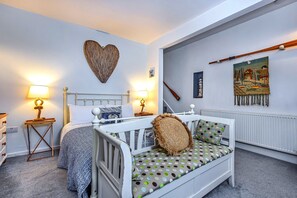 A bedroom with a bed, bedside tables, a wall-mounted heart decoration, a painting, and a wooden musical instrument. - Seaside Cottage Near Whitby Abbey (Whitby)