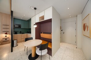 A modern kitchen with a dining area, including a round table and chairs, a pendant light, and a wall-mounted shelf. - Sleek Studio w/ Burj Khalifa View (Dubai)