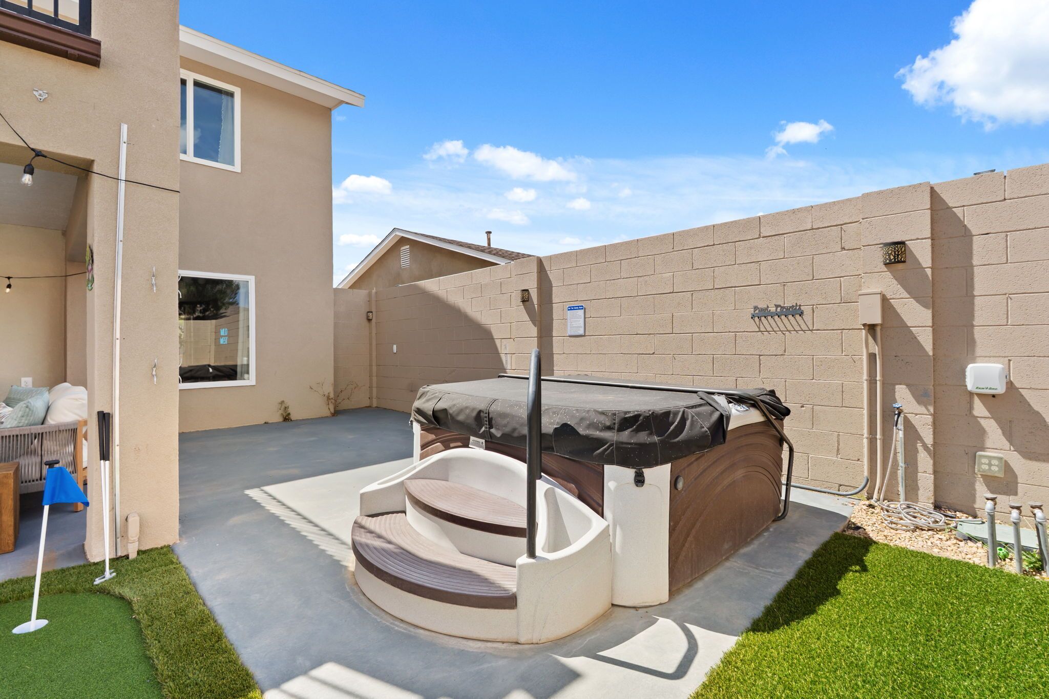 Ein überdachter Whirlpool mit Stufen, eine Terrasse mit Rasenfläche und eine Backsteinmauer.