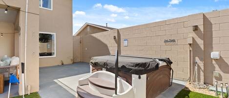 Un jacuzzi extérieur couvert, accessible par des marches, une terrasse avec une pelouse et un mur en briques.
