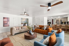 A modern living room with a sofa, armchairs, a coffee table, and a ceiling fan. - Dream Escape! Heated Pool, Hot Tub, Game Room, Golf, Outdoor Paradise! Sleeps 14 (Albuquerque)
