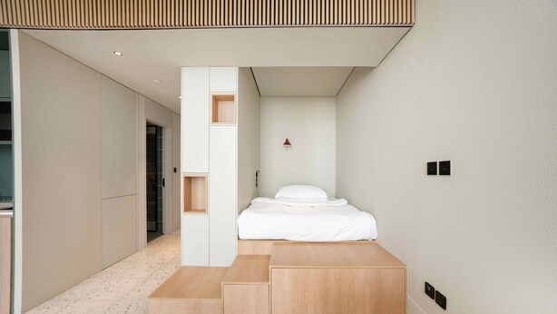 Ein modernes Schlafzimmer mit Bett, Einbauschränken und einer kleinen Sitzecke.