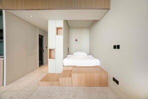 A modern bedroom with a bed, a small bedside table, and a red wall-mounted light. - Upscale Business Bay Studio w/ Pool (Dubai)