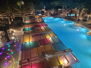 A swimming pool with a deck area, palm trees, and string lights.