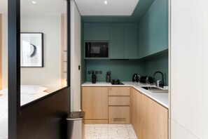 A compact hotel room with a bed, a kitchenette, a microwave, a coffee machine, and a trash bin. - Prime Business Bay Studio | Burj View (Dubai)