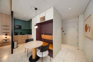 A modern kitchen with a microwave, sink, and cabinets. There is a dining area with a table and chairs. - Prime Business Bay Studio | Burj View (Dubai)