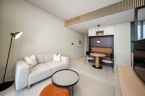 Ein modernes Wohnzimmer mit einer Couch, einem runden Couchtisch, einer Stehlampe und einem Essbereich mit Tisch und Stühlen.