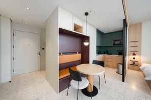 A compact hotel room with a kitchenette, a dining area with a round table and chairs, and a separate sleeping area with a bed. - Bright Studio w/ Iconic Burj View (Dubai)