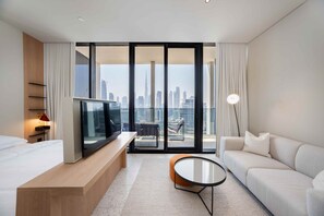 Ein modernes Hotelzimmer mit einem großen Bett, einem Fernseher, einer Sitzecke und einem Balkon mit Blick auf die Stadt.