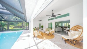 A modern indoor pool area with a glass ceiling, wicker furniture, and a view of the outdoors. - Elegant Bonita Springs Home - Pool, Beaches, Golf & Dining Nearby (Bonita Springs)