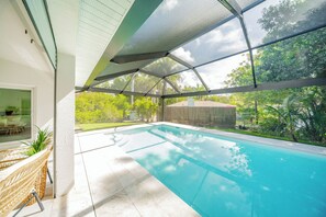 A swimming pool with a glass enclosure, surrounded by a patio area with outdoor furniture. - Elegant Bonita Springs Home - Pool, Beaches, Golf & Dining Nearby (Bonita Springs)