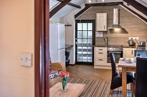 Una cocina moderna con horno integrado, un área de comedor con mesa y sillas, y vista del salón a través de un vidrio.