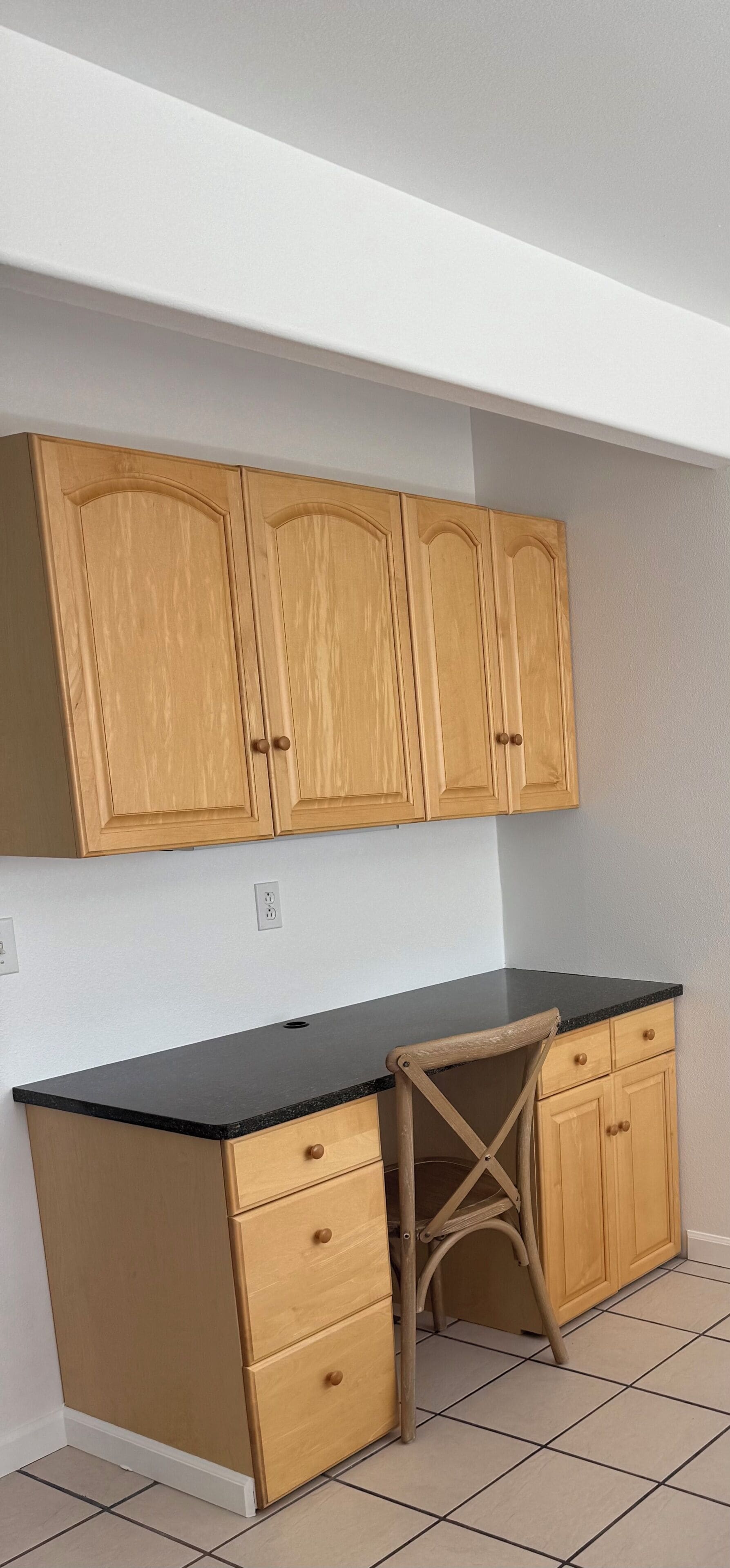 A kitchen with wooden cabinets, a black countertop, and a chair.