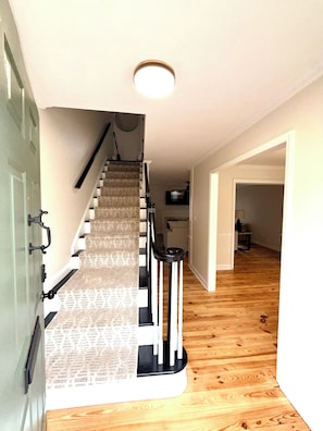 Una escalera con alfombra estampada de periódico, barandilla y lámpara colgante.