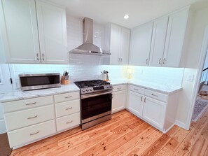 A kitchen with white cabinets, a stainless steel range hood, a microwave, and a gas stove. - 3-bedroom townhome in pleasant Charlotte with AC and charm (Charlotte)