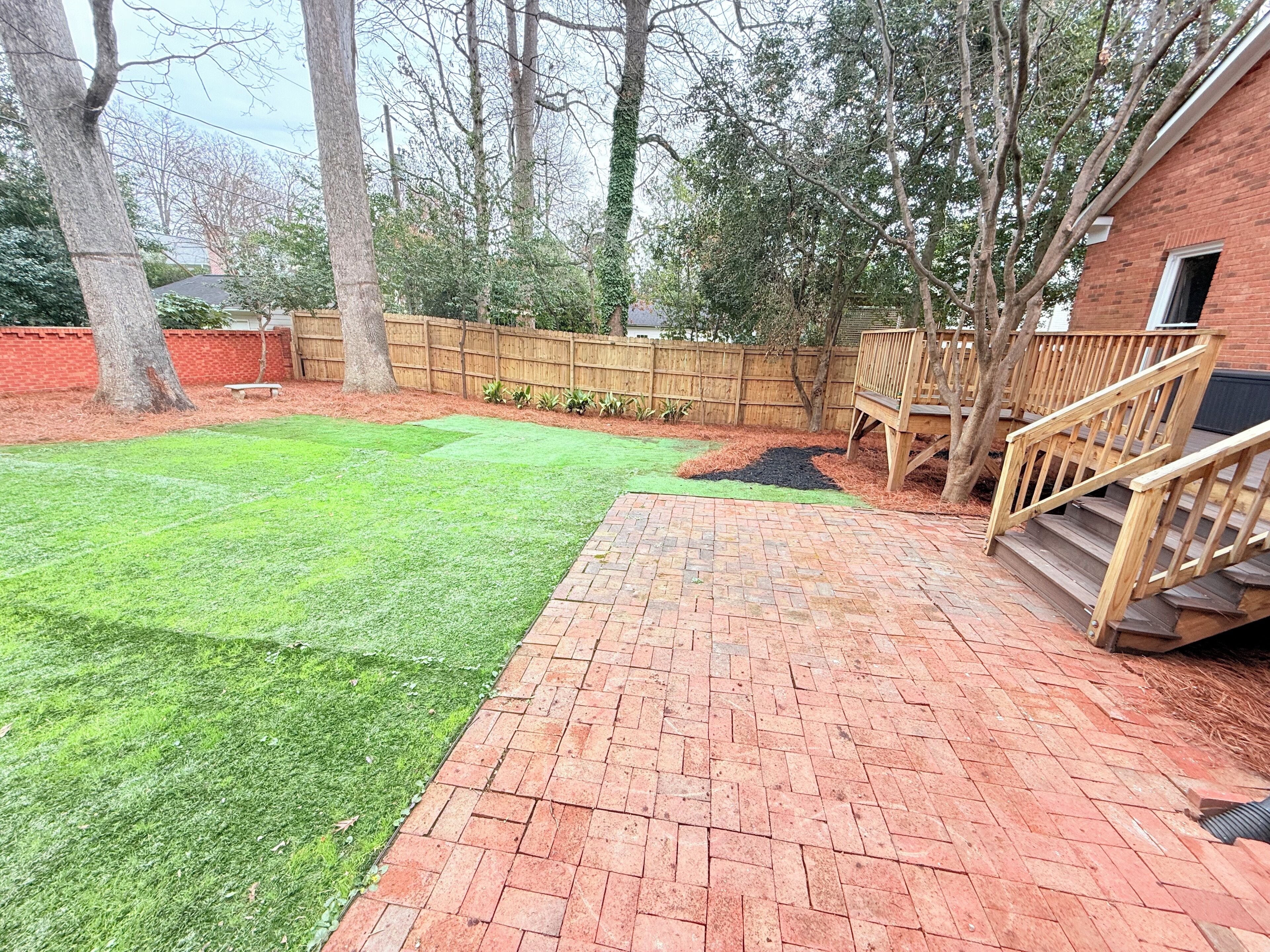A backyard with a brick patio, a wooden deck, and a wooden fence.