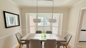 Une salle à manger avec une table en marbre, six chaises, un vase et une suspension.