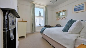 Ein Schlafzimmer mit einem Bett, einer Kommode, einem Fenster mit Vorhängen, einem Spiegel und einem Bild an der Wand.