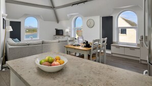 Eine moderne Küche mit Kochinsel, ein Essbereich mit Tisch für zwei Personen und eine Wohnbereich mit einer Couch.
