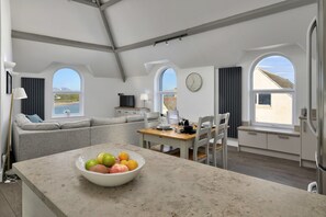 Eine moderne Küche mit Kochinsel, ein Essbereich mit Tisch für zwei Personen und eine Wohnbereich mit einer Couch.
