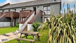 A two-story house with a wooden staircase, a balcony, and a garden with a picnic table. - Luxury Cornish Countryside Hut for 2 (Bude)