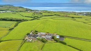 A rural property with a large house surrounded by fields, a swimming pool, and a view of the sea. - Luxury Cornish Countryside Hut for 2 (Bude)