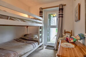 Una habitación con literas, una mesa de madera adornada con un mantel y una ventana con cortinas.