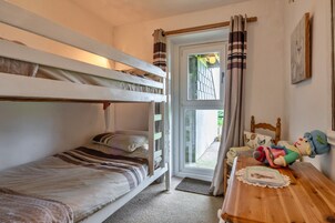 Una habitación con literas, una mesa de madera adornada con un mantel y una ventana con cortinas.