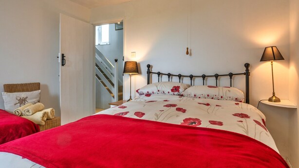 A bedroom with a bed, two bedside lamps, a nightstand, a chair, and a staircase leading to another room. - Luxury Cornish Countryside Hut for 2 (Bude)