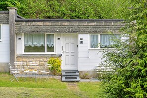 A white cottage with a stone chimney, a front door, and a small porch with a table and chairs. - Camelford Base Near Beaches (Camelford)