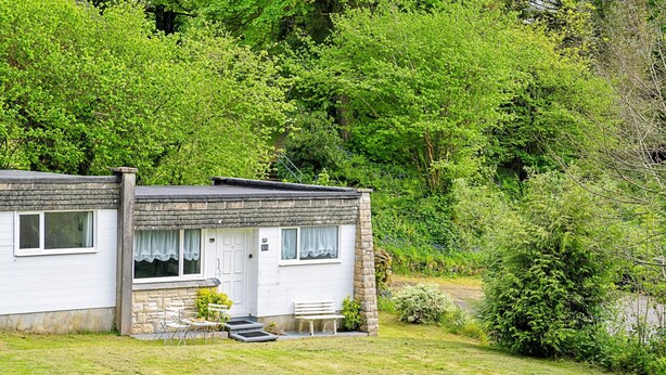 Uma casa de dois andares com fachada de pedra, um alpendre com um banco e um pequeno jardim.