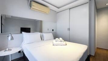 Quarto de hotel moderno com uma cama, mesa de cabeceira com abajur, espelho e guarda-roupa.
