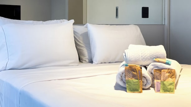 Ein Hotelzimmer mit einem ordentlich bezogenen Bett, Kissen und Pflegeprodukten.