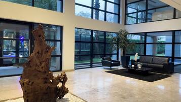 A spacious lobby with a large wooden sculpture, a black leather sofa, and a potted plant.