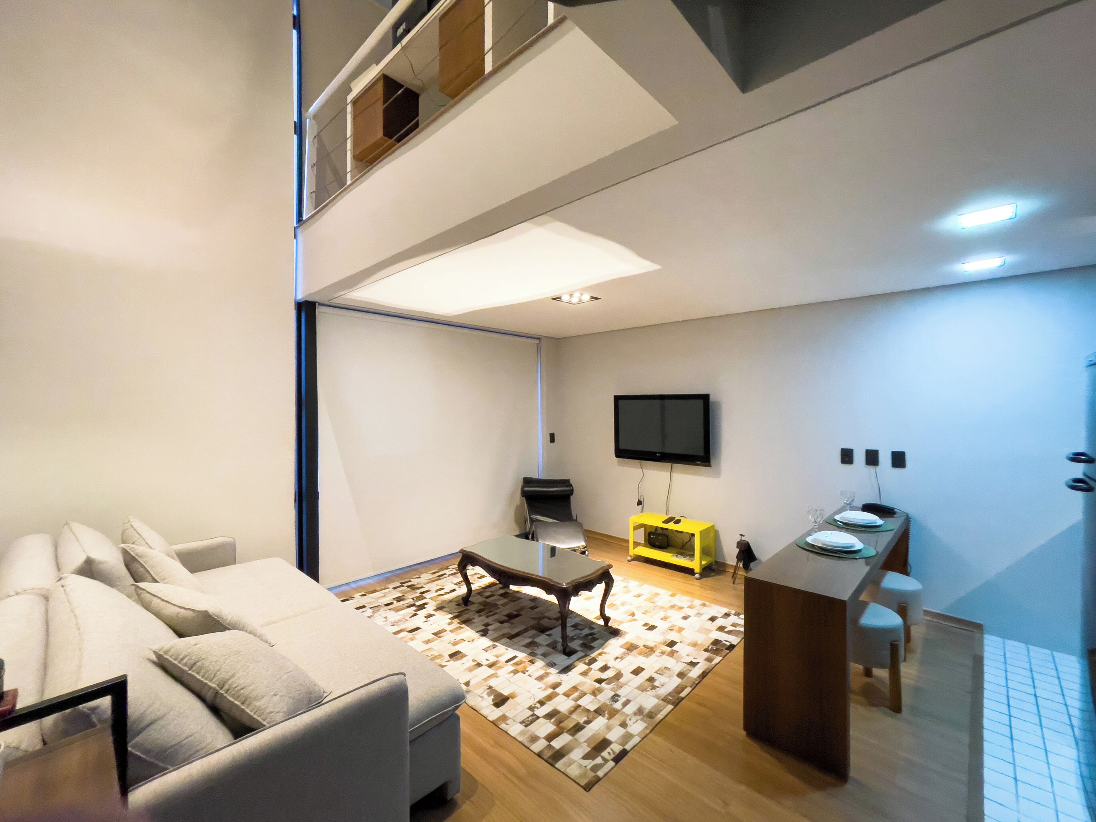 Una sala de estar moderna con un sofá, una mesa de centro, un televisor y una cocina con una barra y taburetes.