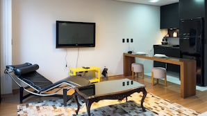 Ein modernes Wohnzimmer mit Flachbildfernseher, einer Couch, einem Couchtisch und einer Küchenzeile mit Kühlschrank und Herd.